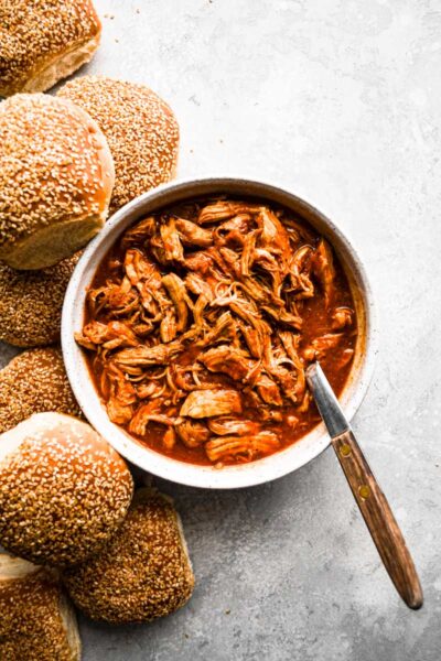 Pulled BBQ Chicken in a bowl next to Sesame Seed buns