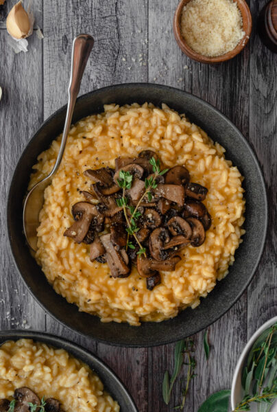 pumpkin with rice topped with mushrooms and herbs with a spoon in a gray-black plate bowl