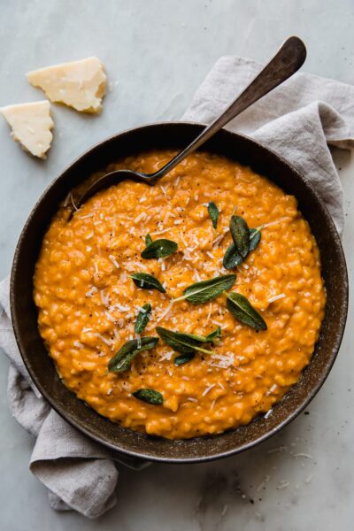 creamy squash risotto topped with shredded cheese and herbs in a bowl plate