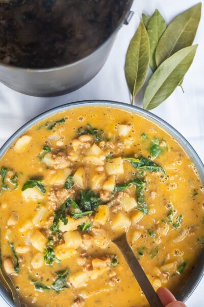 cooked pumpkin stew with meat, kale, potatoes and white beans in a pot