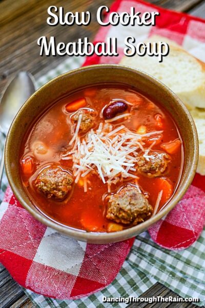 orange reddish colored soup with meatballs, beans and veggies topped with parmesan cheese in a brownish pot