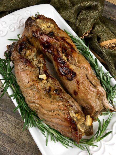 roasted pork tenderloin stuffed with mixture of apples, feta cheese, and herbs garnish with rosemary on a white servind dish