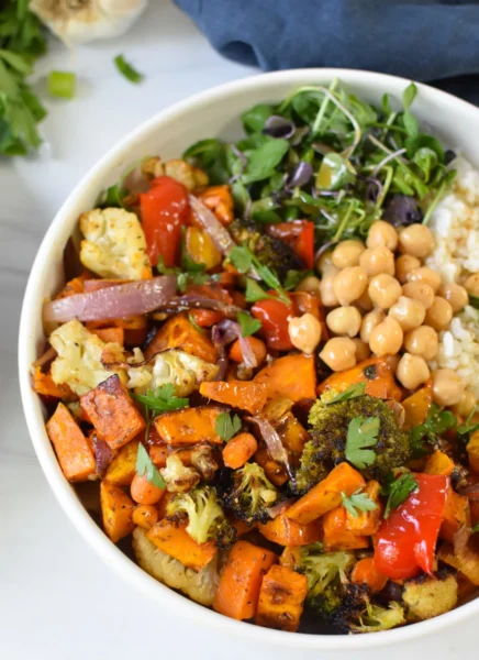 Sweet Potato Bowl with roasted sweet potatoes and vegetables, grains, greens, chickpeas drizzled dressing in a white bowl