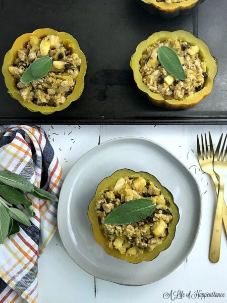 acorn stuffed with cooked ground meat, apples, and raisins, garnished with sage leaf on a white plate