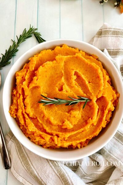 mashed sweet potato topped with rosemary in white bowl with a poon on the side