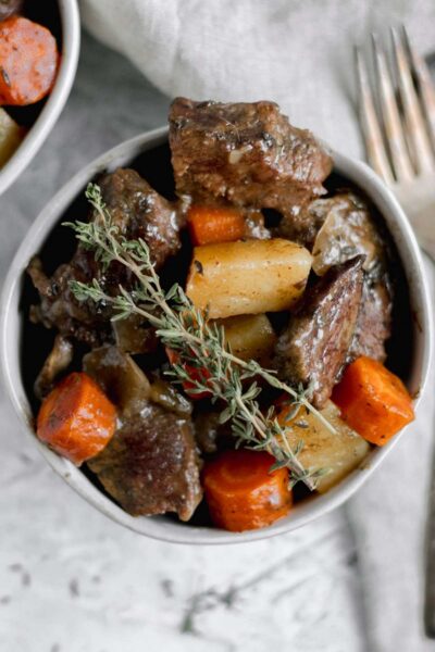 cooked cube beef with carrots, potatoes and celery in a white bowl