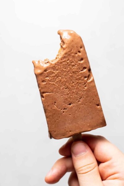 a hand holding a  single bitten creamy dairy chocolate banana popsicle