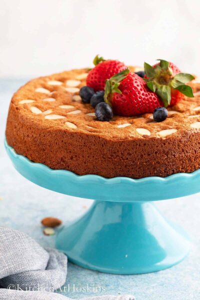 bake round almond flour cake topped with strawberries and blueberries on a blue cake turntable