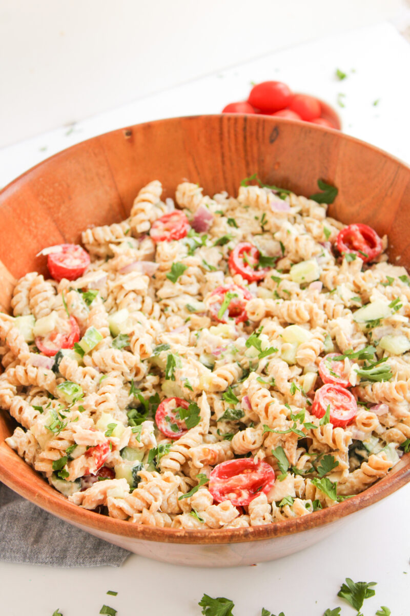 Angled view of tuna pasta salad in wood bowl with blue napkin behind it.