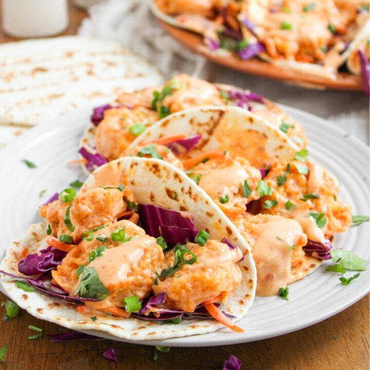 3 bang bang shrimp tacos in a row on a small plate