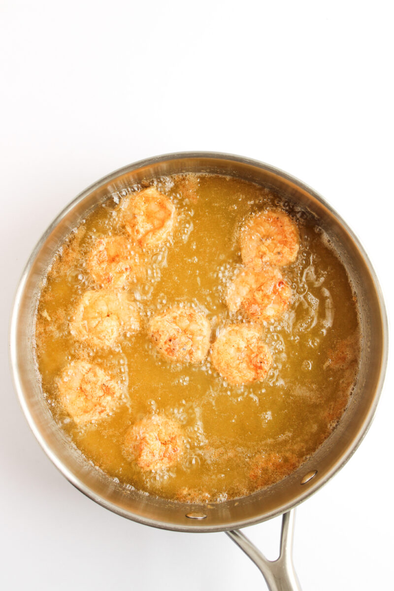 Battered shrimp frying in oil in a silver frying pan