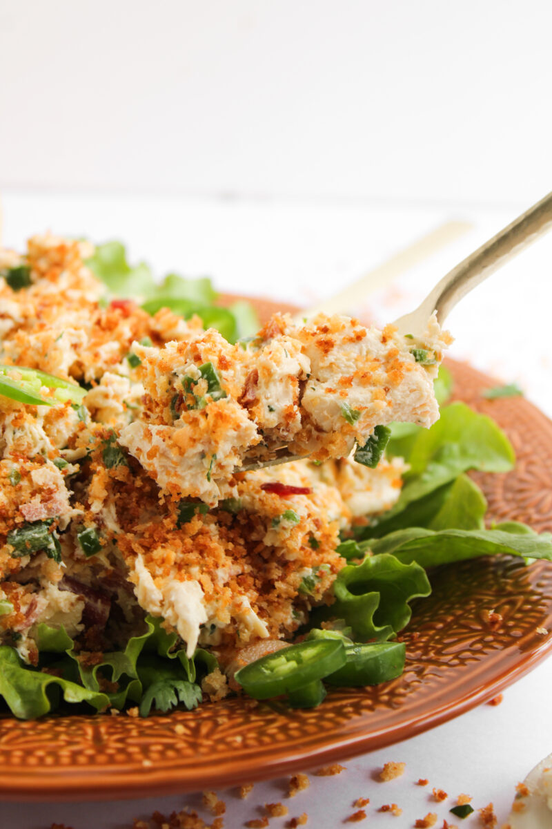 Gold fork picking up a bite of chicken salad with lettuce and orange plate out of focus in the background.