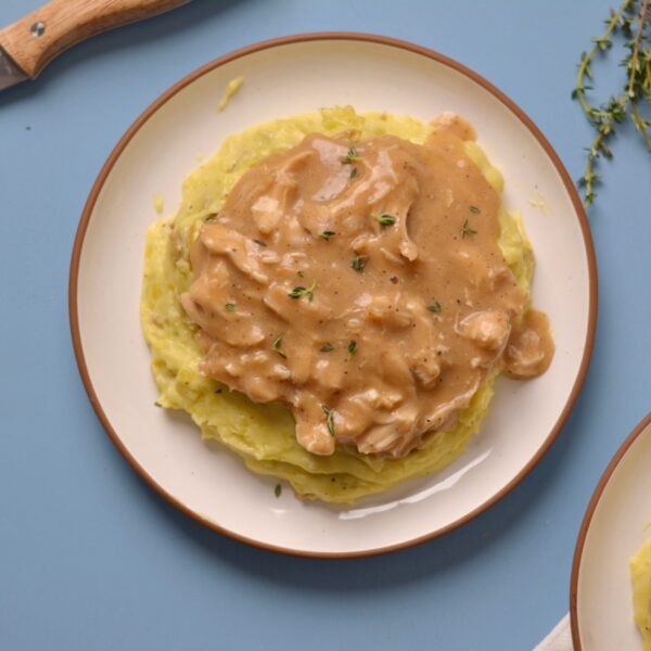cooked chicken and gravy over mashed potatoes on a white plate