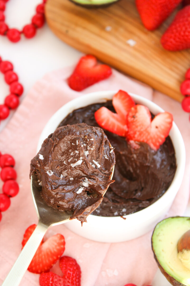 Gold spoon scooping chocolate pudding with white bowl filled with pudding and strawberries in the background.