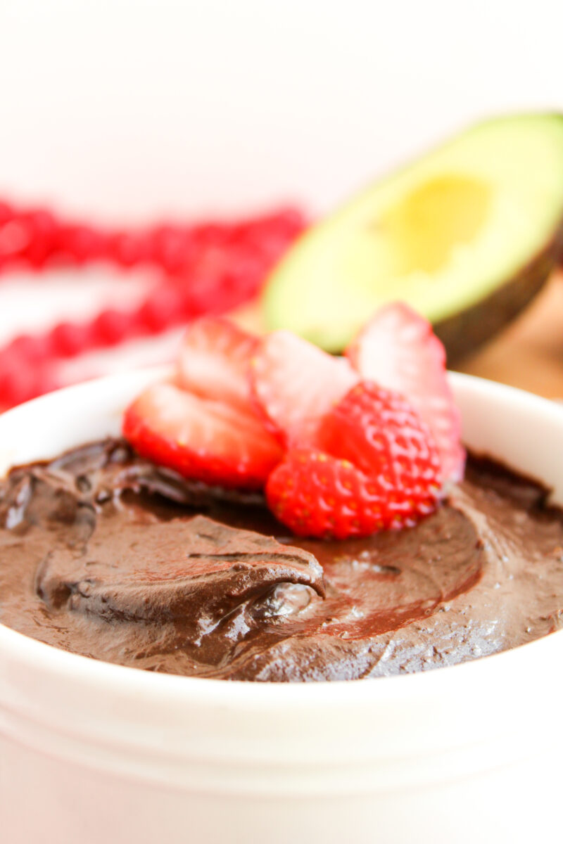 Close up of creamy chocolate pudding with heart shaped strawberries in the back.
