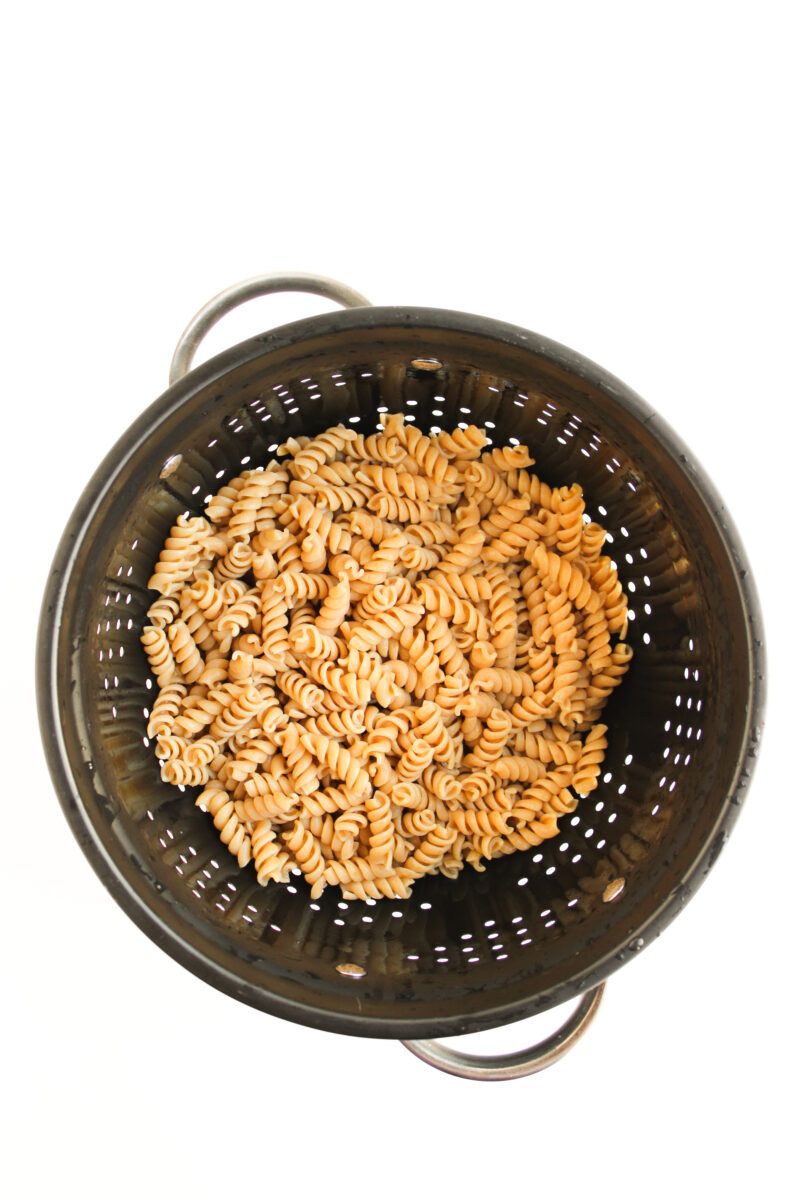 Cooked pasta in a black strainer with white background
