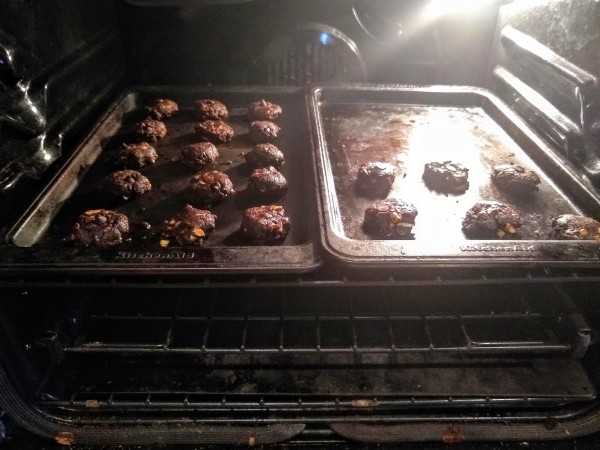 cookie sheets with chocolate cookies side by side in oven.