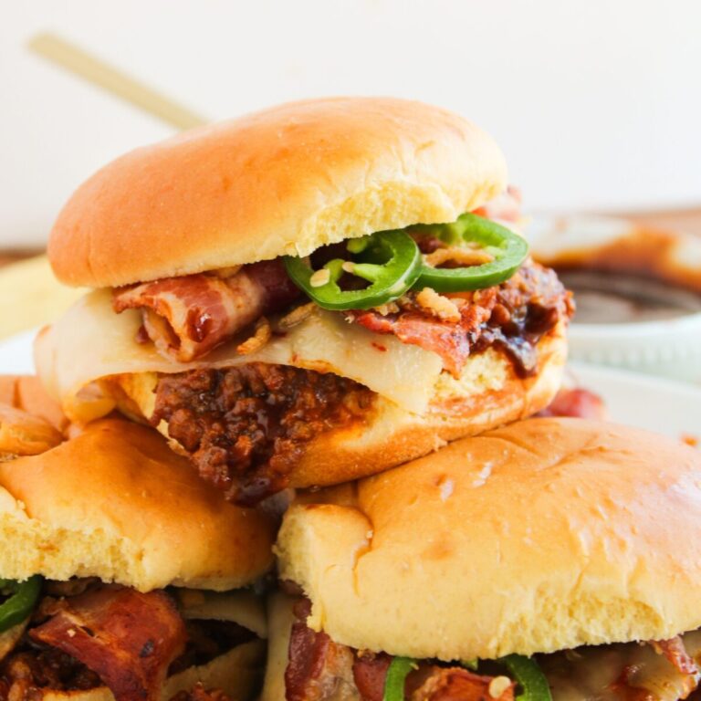 Sloppy Joes in a pile on white plate with bowl of BBQ sauce in the background.