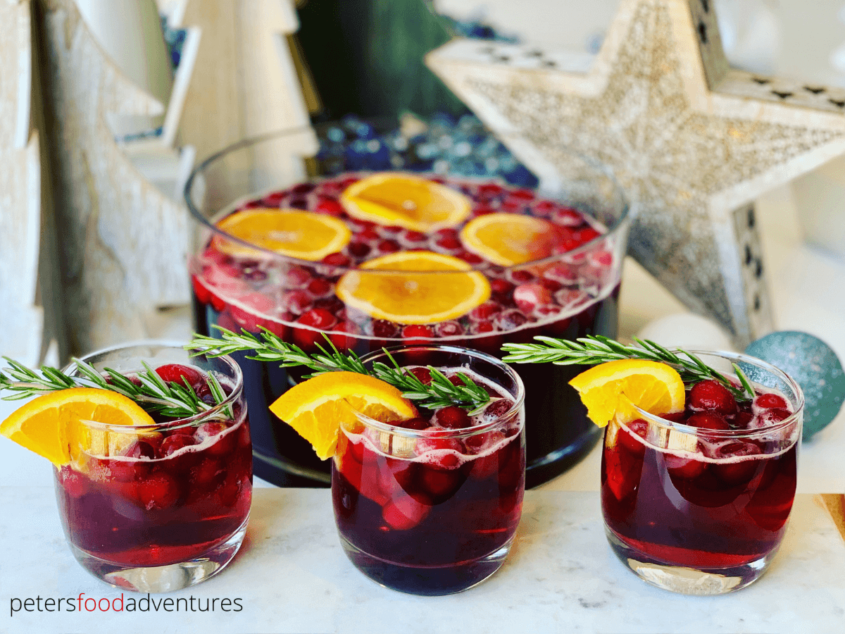 nonalcoholic Christmas punch with cranberries, orange slices, and sprigs of rosemary in a punch bowl and small glasses