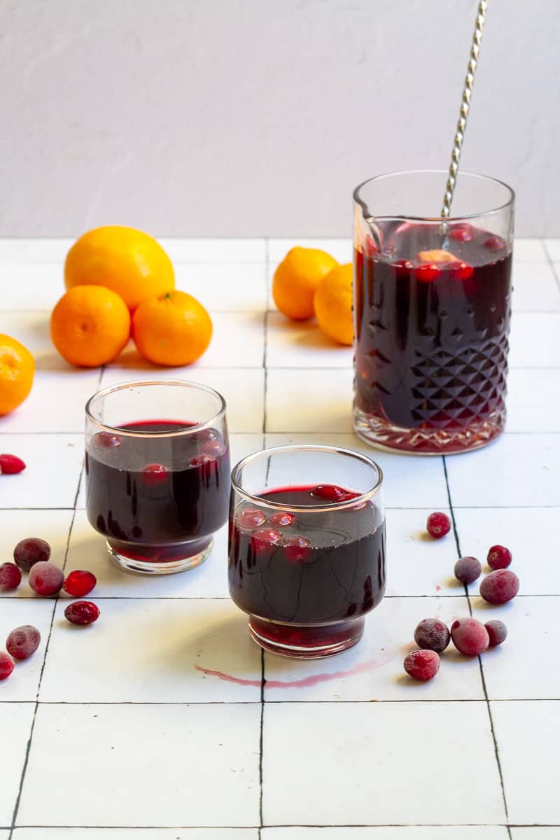 cranberry orange sangria in big and small glasses on white counter with cranberries and oranges