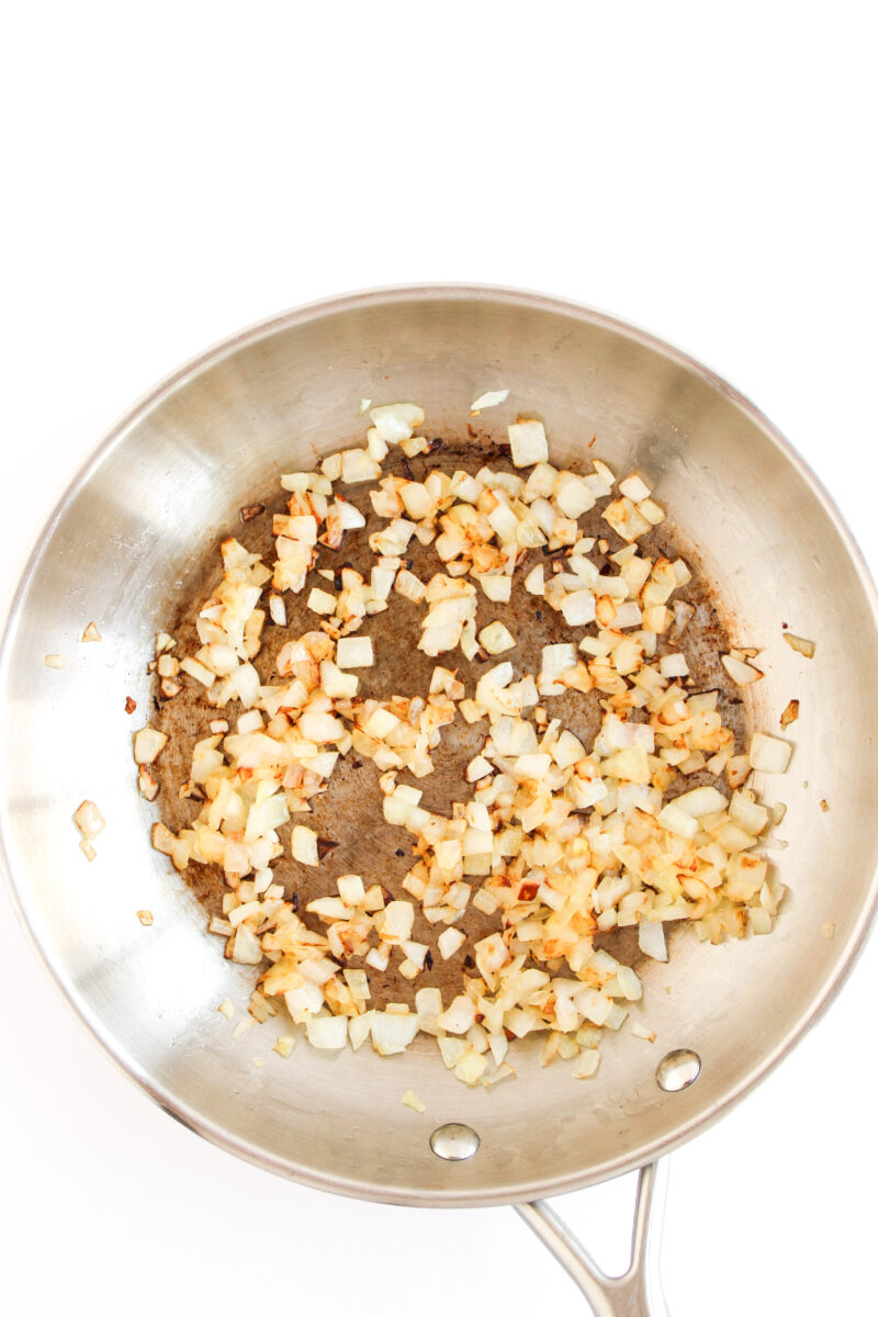 Cooked onions in a silver skillet on a white background.