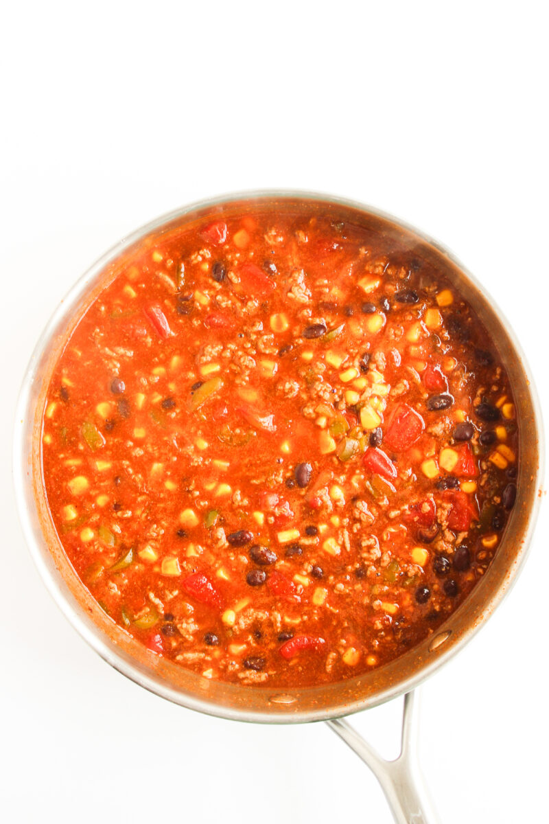 Beef enchilada casserole filling in a silver pan with white background.