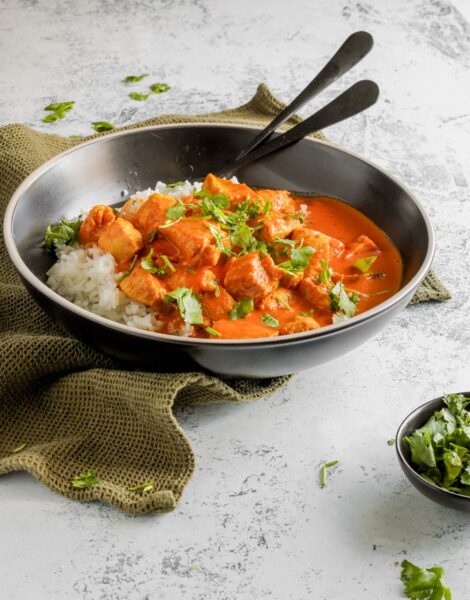 cooked cube chicken in a creamy orange sauce served over rice in a gray bowl