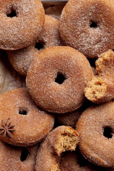 close up image of baked gluten-free apple cider donuts coated with sugar, cinnamon and all spice, some whole and some bitten off/halved