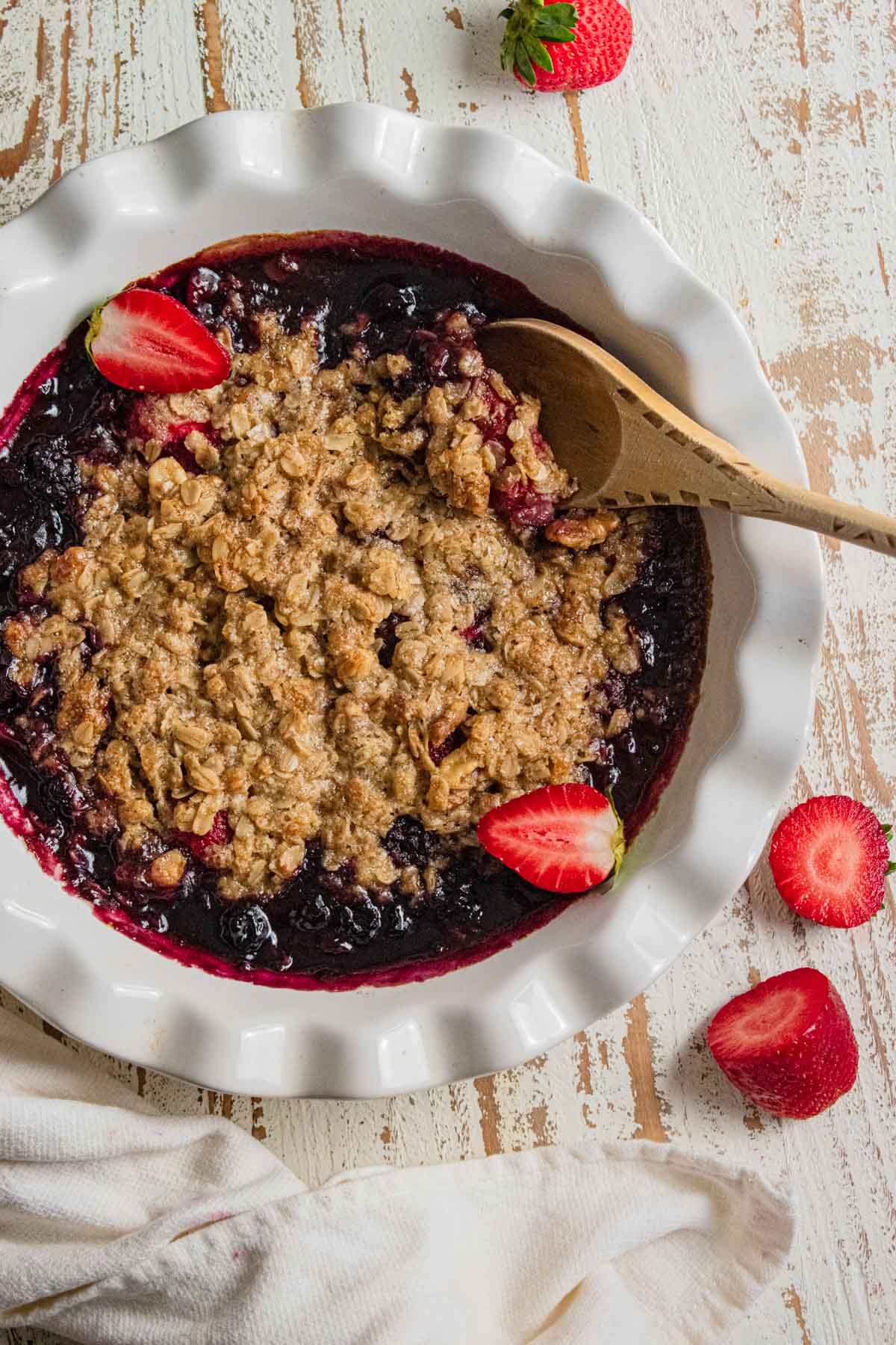 fruit oatmeal crisp with strawberries, and blueberries with a wooden spoon in a white bowl