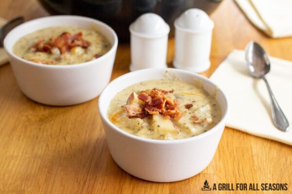 potato soup topped with bits of bacon in small white bowls with a spoon on the side
