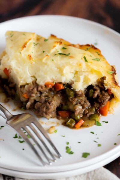a slice of cooked shepherd's pie made with ground meat and vegetables topped with a layer of cheese in a white plate