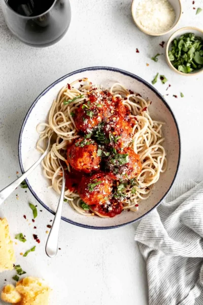 meatball with tomato sauce over spaghetti pasta woth forks on a blue rimmed white bowl-plate