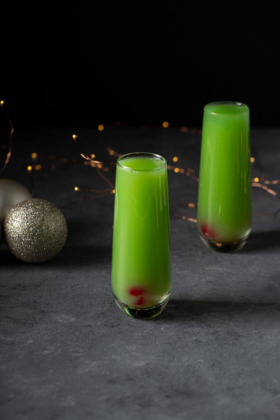 Grinch Mimosas with a maraschino cherry plunked into the bottom of the champagne flute, with festive decorations