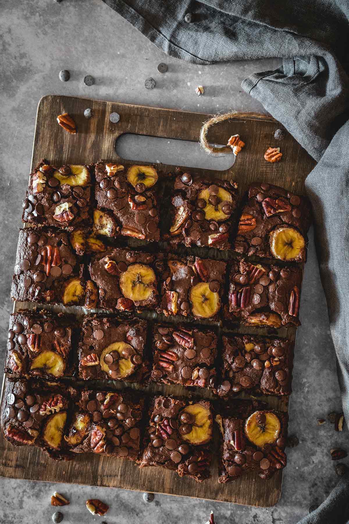 chocolate lentil brownies with banana slices, chocolate cips and chopped pecans on a wooden boeard