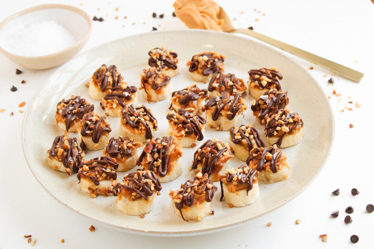 Banana snickers bites on sandy color plate with chocolate chips scattered around.