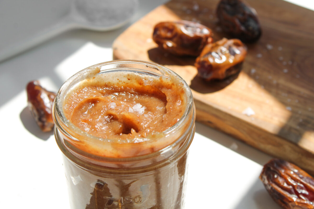 Angled view of date caramel in a clear jar with wood board in the background and more whole dates.