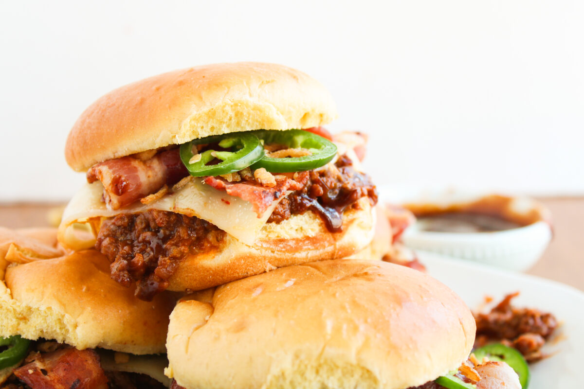 Close up of sloppy joe on top in a pile on a white plate with bowl of BBQ sauce in the background.