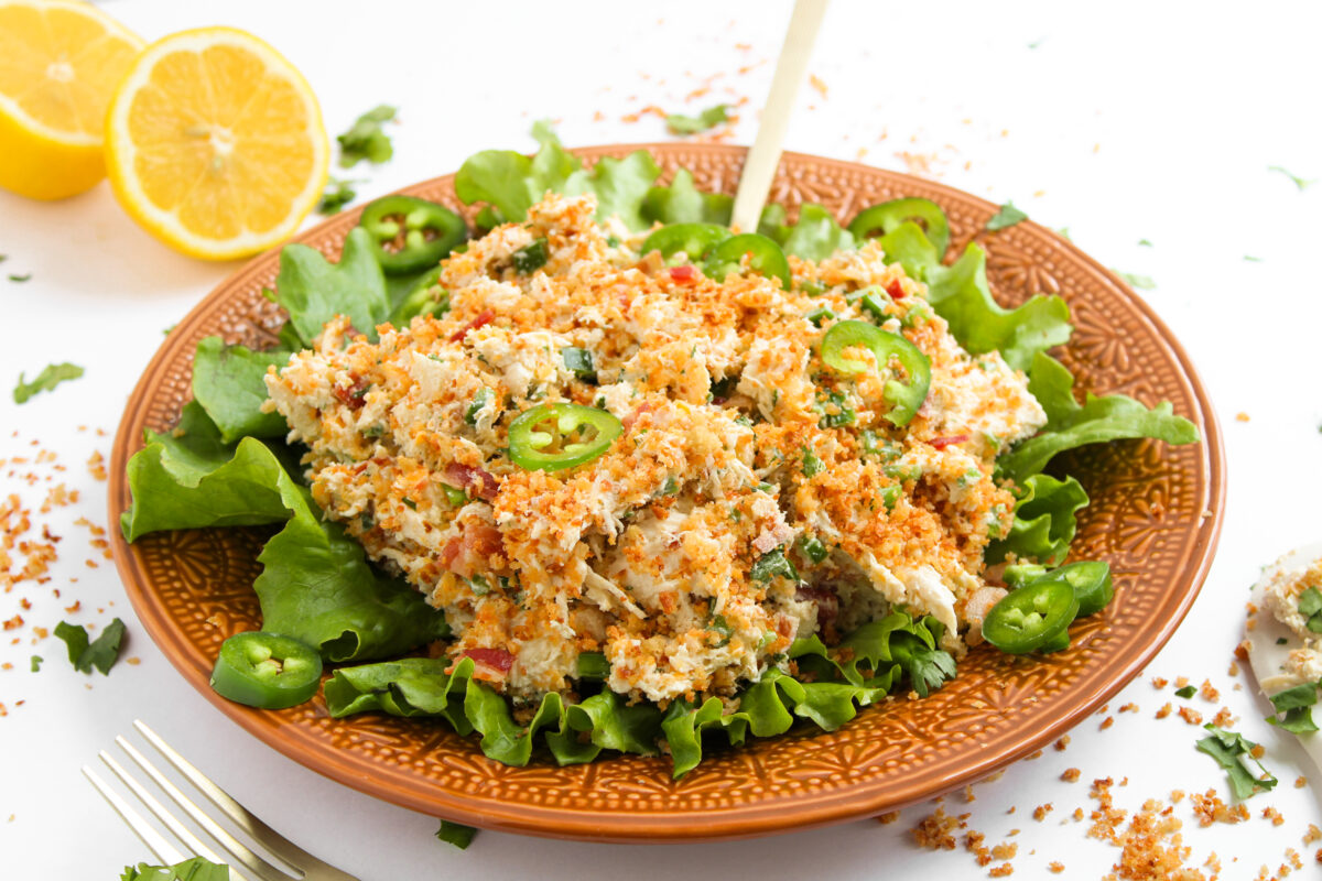Chicken salad on a bed of lettuce on an orange plate with gold fork.
