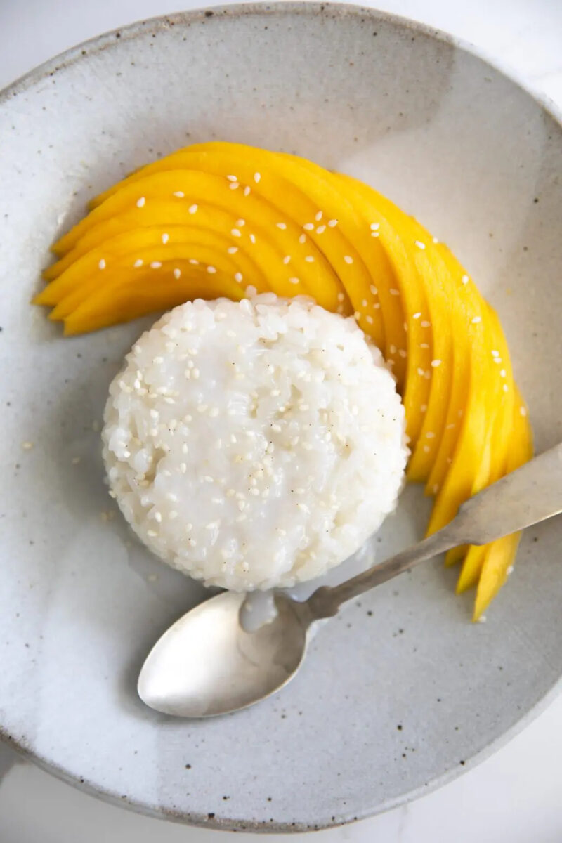 sticky white rice with  mango slices topped with sesame seed with a spoon
