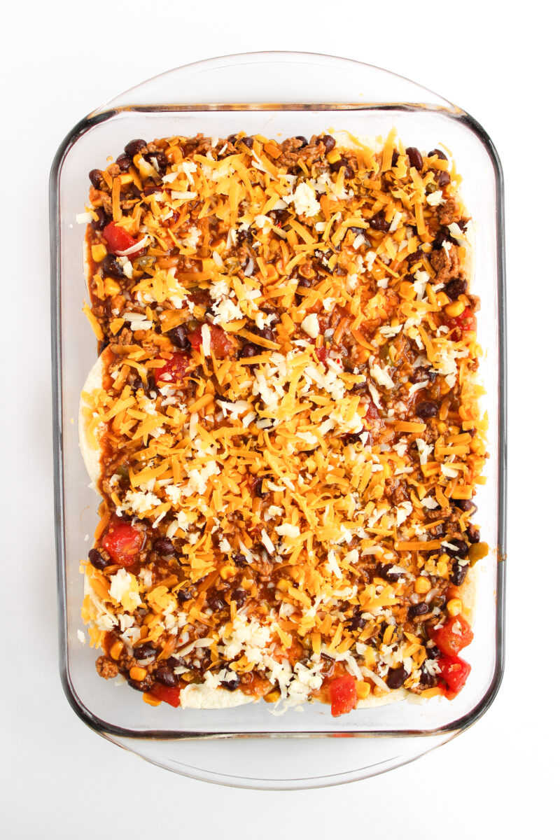 Casserole dish on white background with layered ingredients before baking.