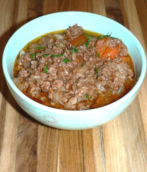 cooked stew made wit ground beef, cabbage, onions and tomatoes garnish with herbs in a white bowl