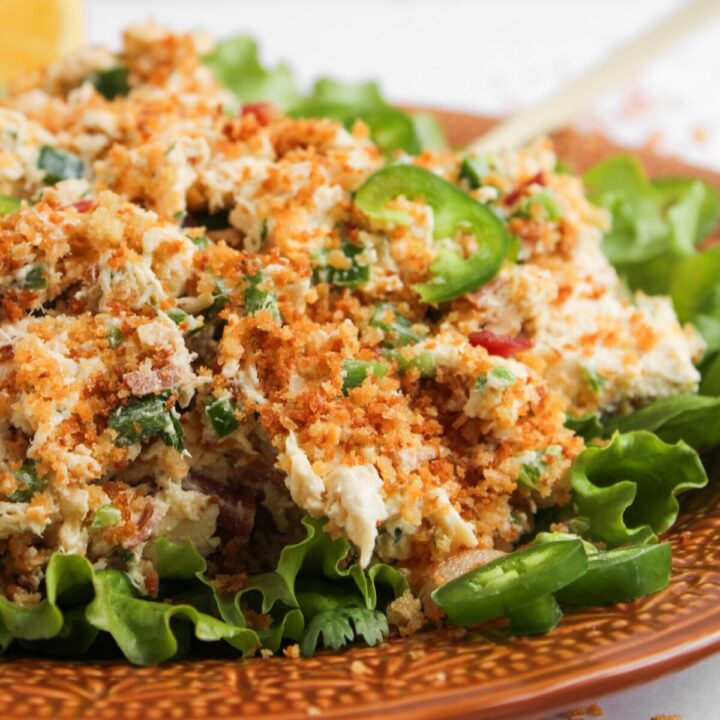 Chicken salad with jalapeño slices on a bed of lettuce on an orange plate.