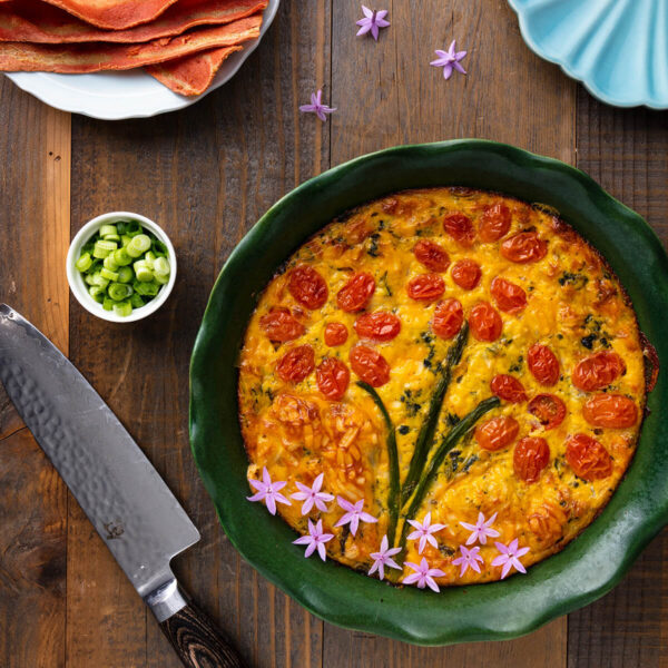 cooked quicke topped with veggies and tomatoes styled in the shape of flowers served in a green circular dish