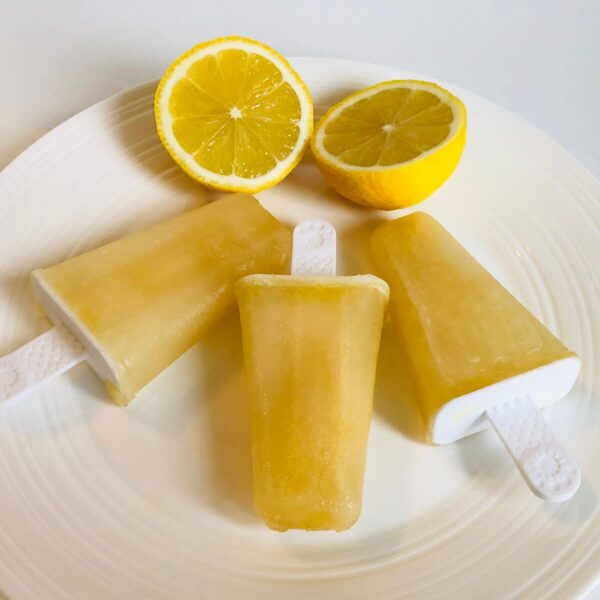 3 lemon popsicles on a white plae with slices of lemon