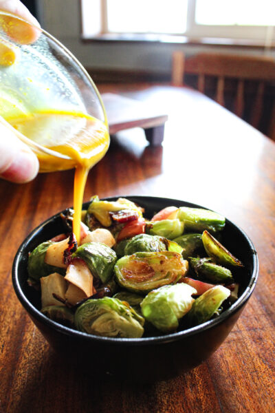 pouring maple mustard sauce over brussels sprouts