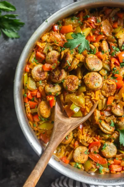 cooked slices of sausages with veggies mix with rice in a skillet with a wooden mixing spoon