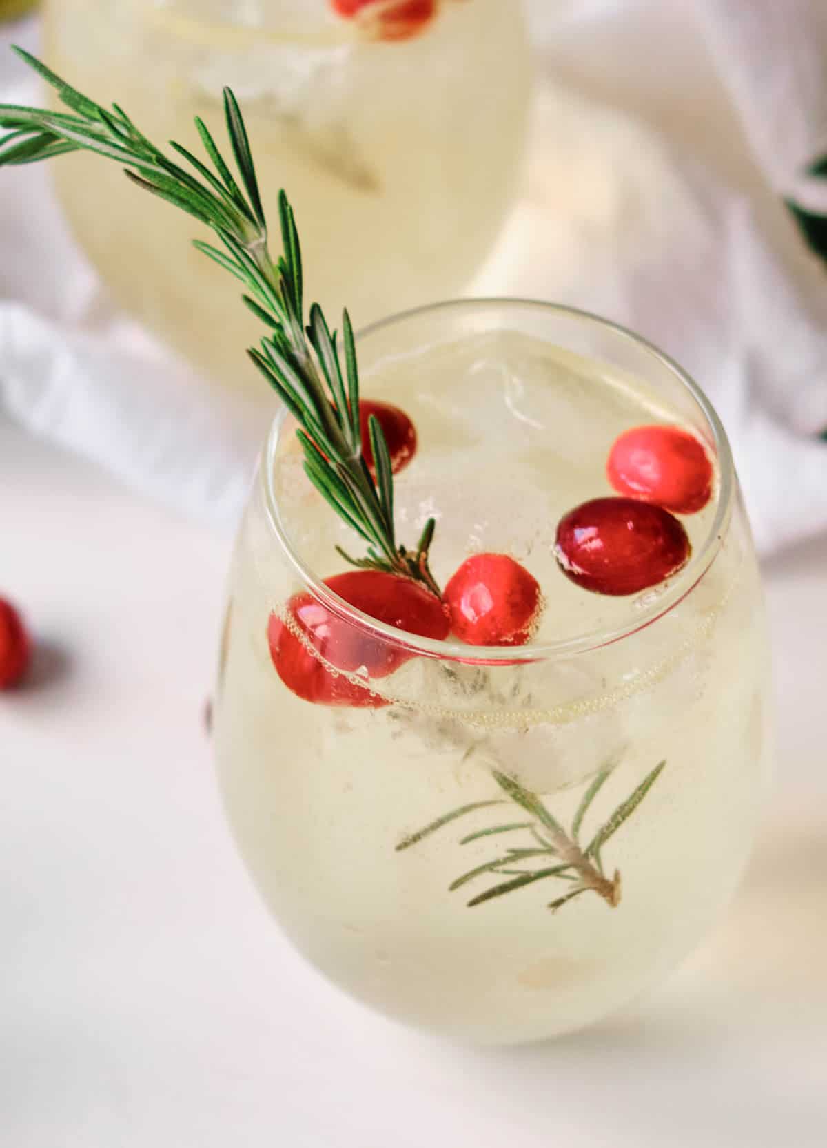 orange mocktail with cranberries, ice and sprig of rosemary in a glass