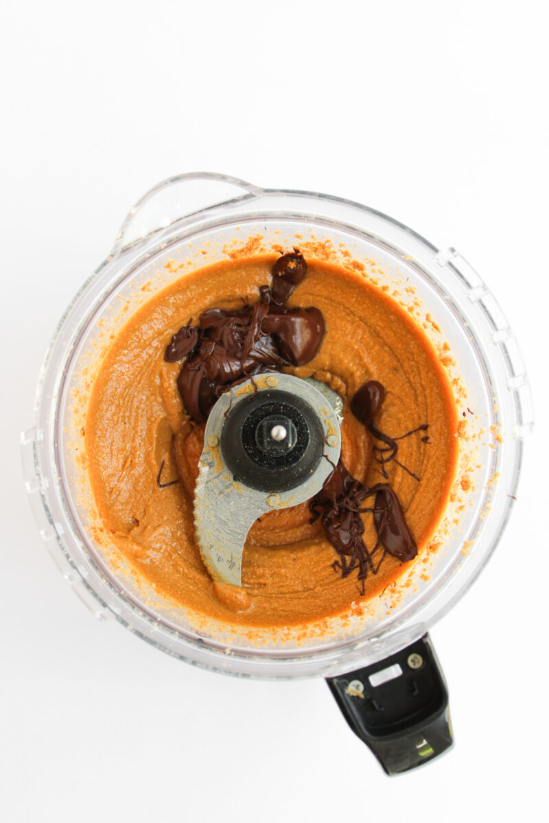 Peanut butter with melted chocolate in food processor on white background.