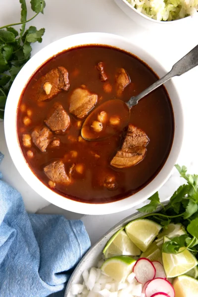 red chili broth stew with pork in a white bowl with a spoon