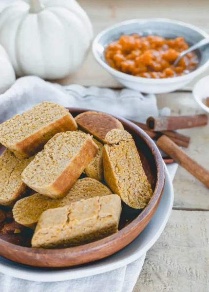 pumpkin biscottis on a wooden saucer plate with cinnamon barks in the background